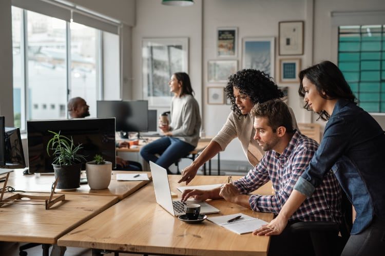 Diverse group of office workers looking at the same laptop together