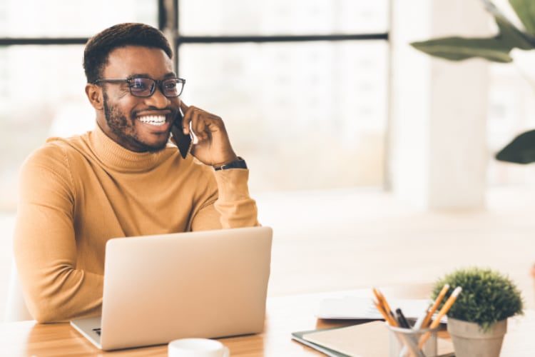 Black man talks on cell phone while working on laptop