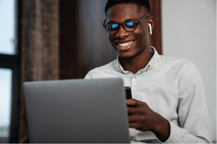 Black man using phone while on computer with earbuds in ears