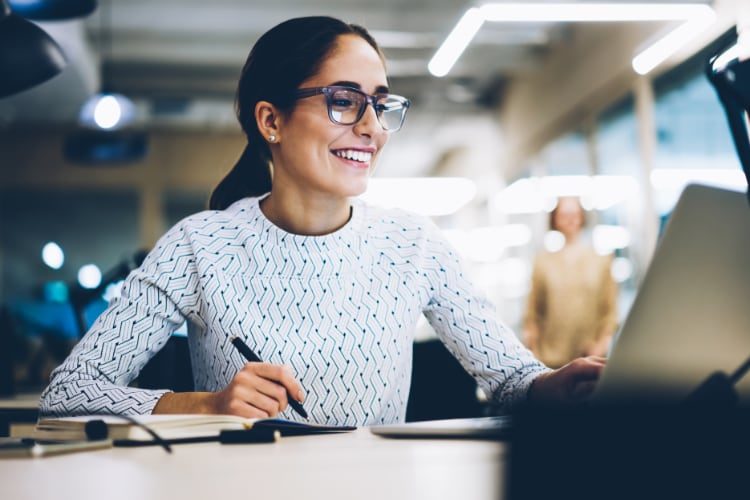 Woman taking notes off of something she sees on a laptop screen