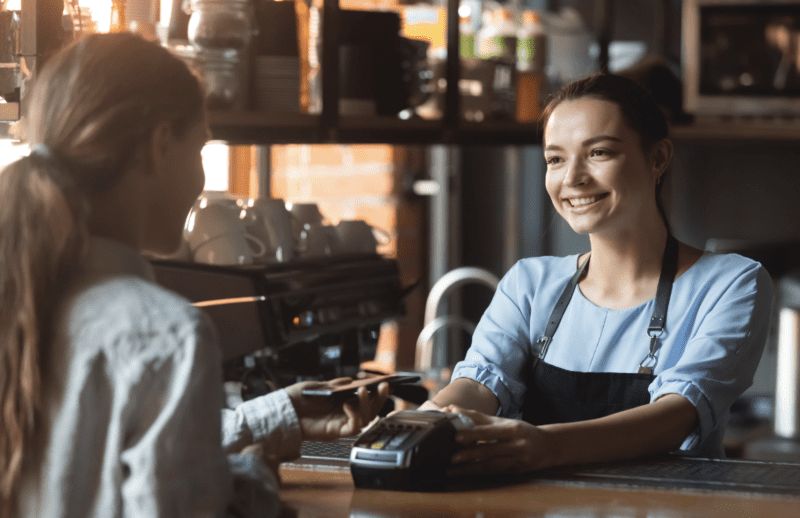 Person behind the counter of a coffee shop assisting a customer with checkout.