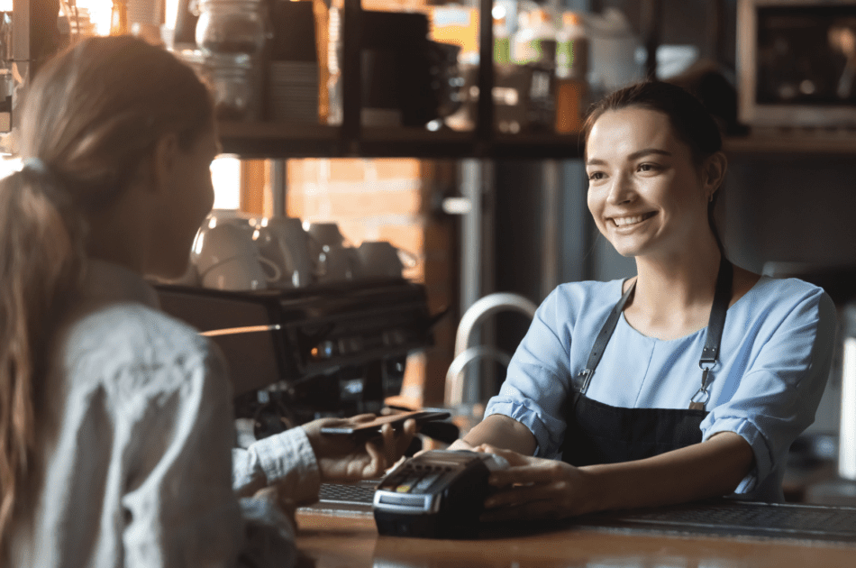 Person behind the counter of a coffee shop assisting a customer with checkout.