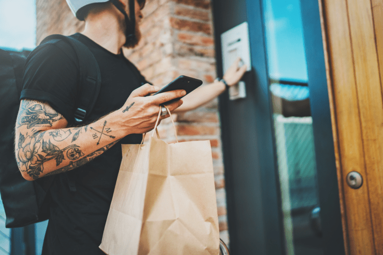 A delivery driver buzzing into an apartment holding a meal delivery in a paper bag