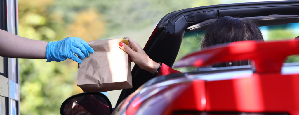 A person in a convertible picking up food at a drive through