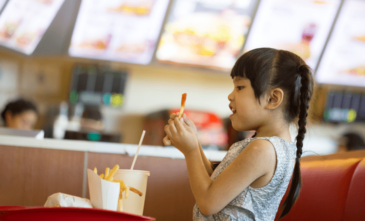 Young girl with braids looking excitedly at a french fry dipped in ketchup