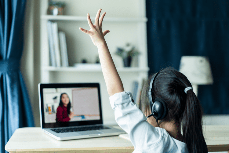 Young girl with hand raised taking class on a laptop