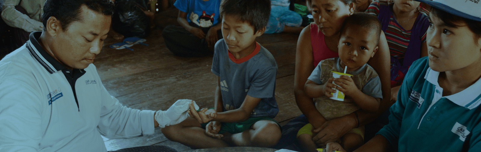 Photo of a pan in sterile gloves interacting with a child while his family looks on