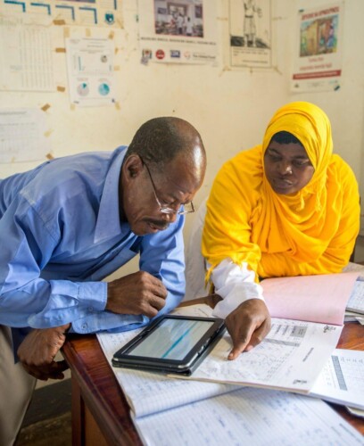 Charawe PHCU, Unguja Island, Tanzania. Public Health Nurse Mosi Ahmada Juma (in yellow) reviews a new malaria case with DSMO Shaabani Khamis, using the MEEDS and MCN system.