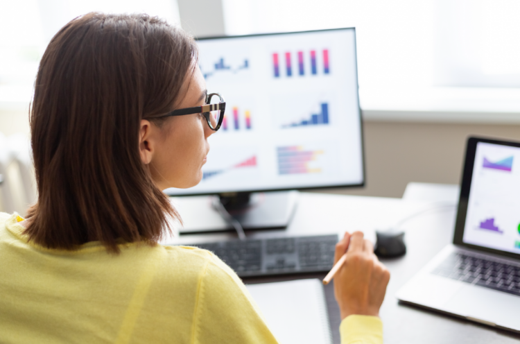 A person from behind works on a computer with data displayed in chart form